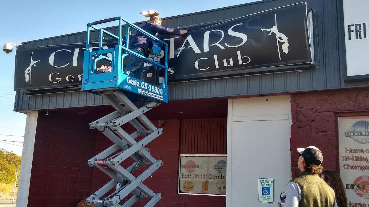 The new owner of the City Stars strip club building in Kennewick, Jared Walther, takes down the sign as members of the Apostolic Center gathered to watch.