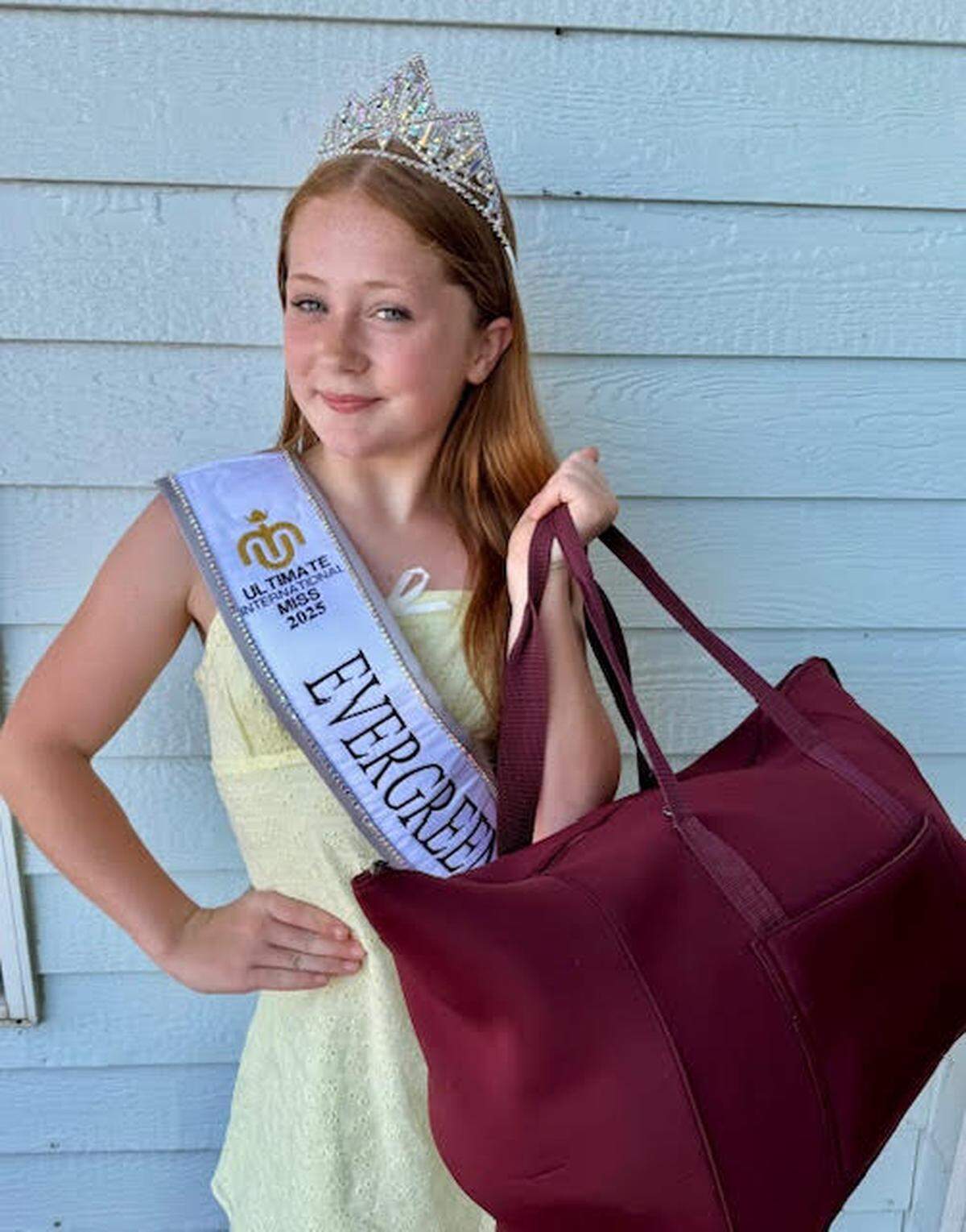 Rhylinn Simmons holding a duffle bag while in her sash and crown.