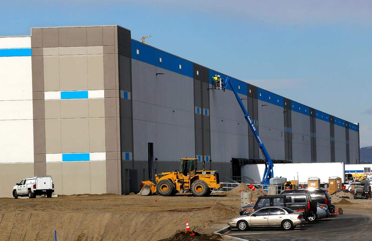 Workers use a boom lift to reach near the top of the Pearl Project building in east Pasco, which is one of the two new Amazon warehouses.