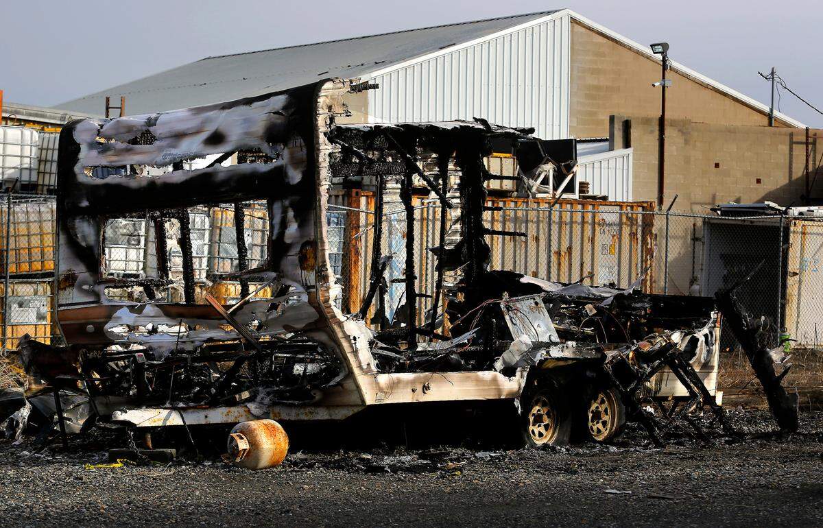 Burnt out shell of a travel trailer abandoned on the shoulder of Railroad Avenue near other motorhomes and trailers in downtown Kennewick in 2023