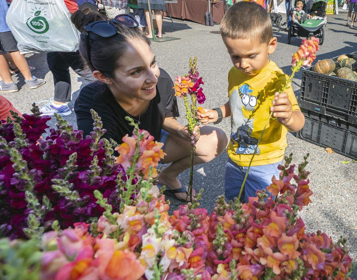 Celina Rathbun, of Pasco, smiles watching her three-year-old son, Dirk, pick Snapdragons from My Garden Over Floweth at the Richland Farmers Market in 2019.