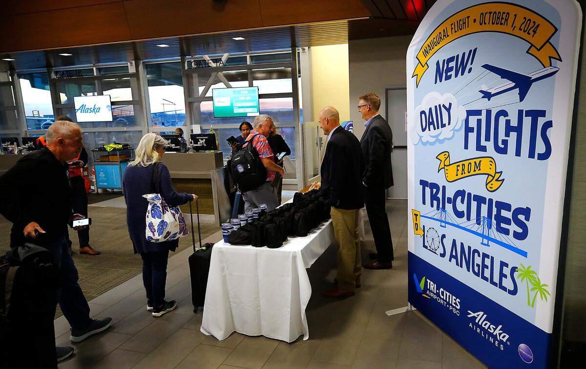 Passengers receive souvenirs from airport director Buck Taft, left, and Karl Dye, president of the Tri-Cities Development Council (TRIDEC), as they board Alaska Airlines’ new daily flight between the Tri-Cities Airport and LAX Tuesday morning in Pasco. The 76-seat Embraer carrying 48 travelers plus crew departed shortly after sunrise.