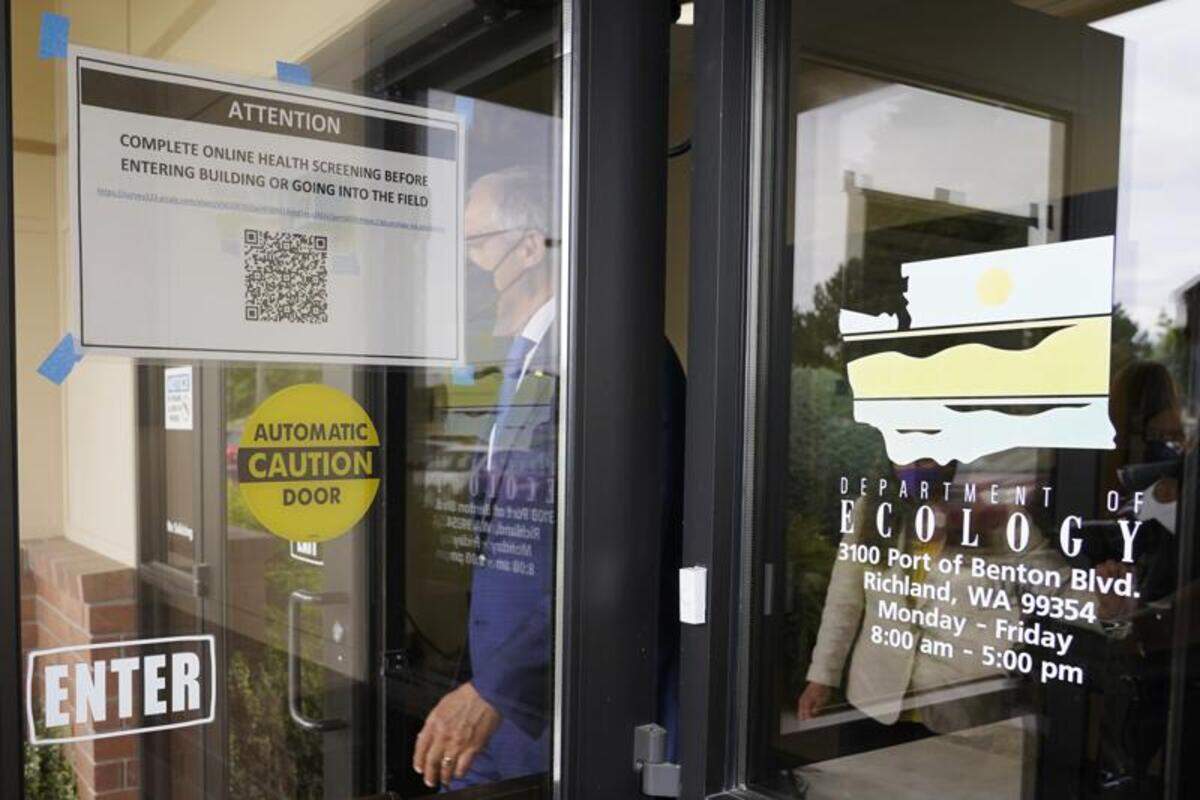 Washington Gov. Jay Inslee walks past a sign asking visitors to complete a health screening as he steps outside to talk to reporters at a Dept. of Ecology office in Richland.