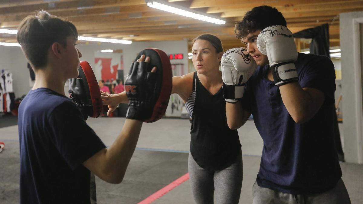 Sarah Howell shows a student a sparring combo inside of her gym in Pasco while another student, Daniel Alvarado, left, holds up the mitts. Howell is a MMA fighter, who also owns two businesses, Wolfpack Fitness and MMA.