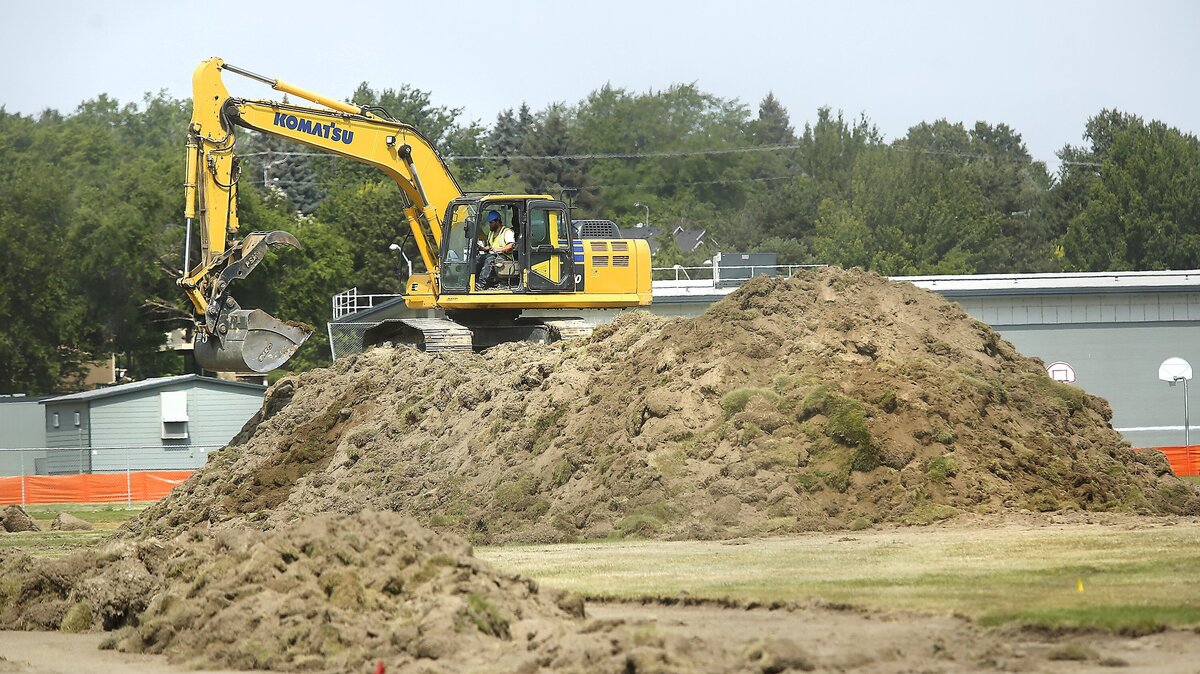 An excavator operator works from the top of a mountain of sod on the south side of Park Middle School in Kennewick. The sod is being scraped off to build a new track and multi-sport playfield at the school on West Tenth Avenue.