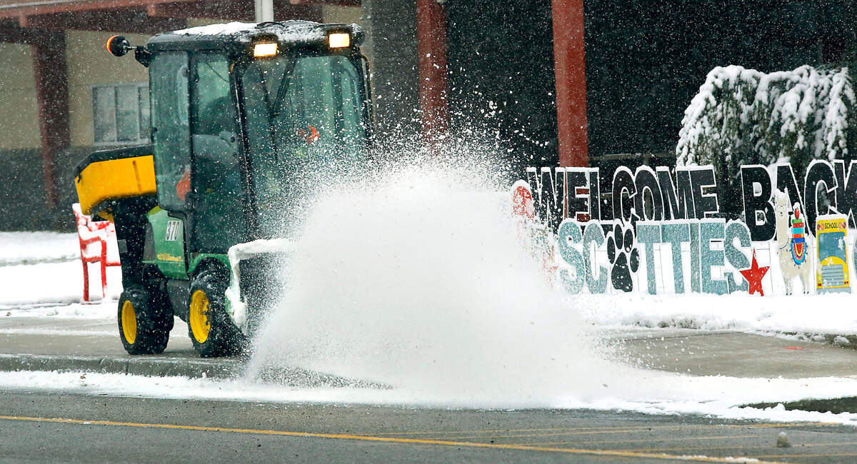 A Kennewick School District employee brushes away snow early Monday morning from the sidewalk in front of Highlands Middle School on South Tweedt Street. Signs in front of the building welcome students back to the classroom for a hybrid in-person learning schedule during the ongoing coronavirus pandemic.
