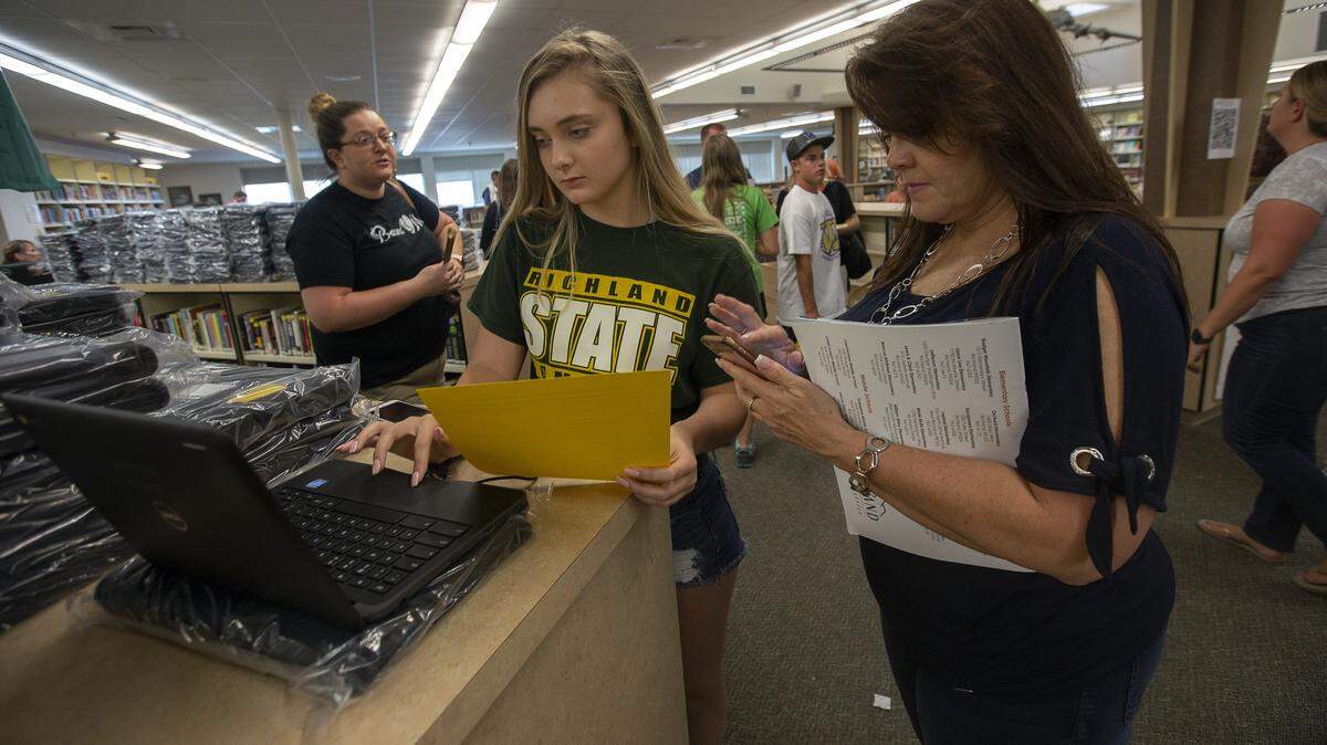 Sophomore Natasha Ford checks to see if her new Google Chromebook is working properly with her mother, Darla Ford, inside Richland High School’s library on Thursday during registration.