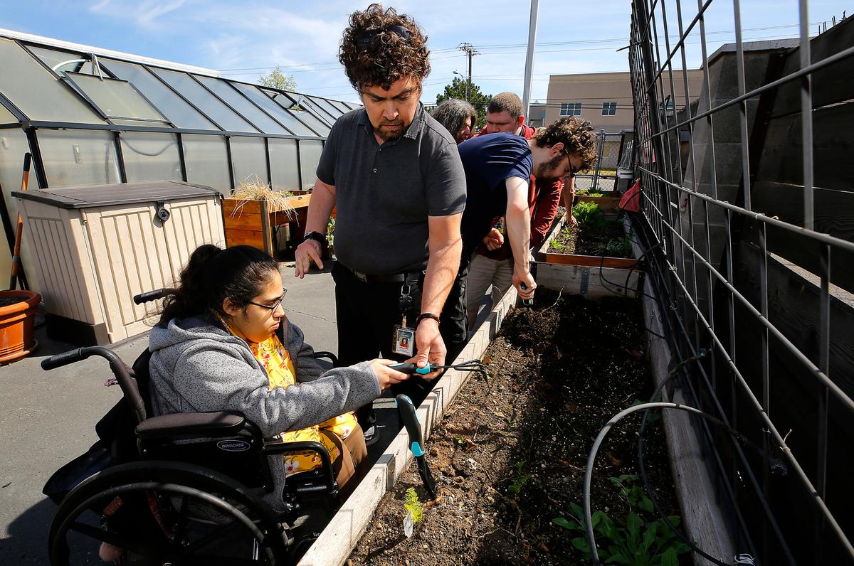 Nathan Plung, Columbia Ability Alliance community center assistant manager, helps clients Sadie Retana, 22, and Chance Kloepper, 23, work the soil in the facility’s outdoor raised garden beds.