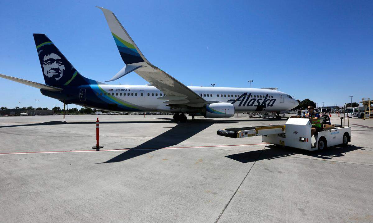 A baggage handler drives equipment past an Alaska Airline jet preparing to depart from the Tri-Cities Airport in Pasco.