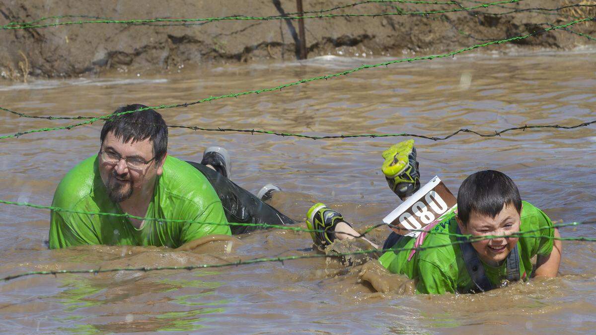 Brendon Highman of Benton City and his son, Dale, crawl in muddy water underneath wires while participating in the Renegade Rage 10k at Hanses Farm in Pasco. Participants could run on four courses: elite competitive 10k, renegade 10k, rager 5k and rebel renegade.