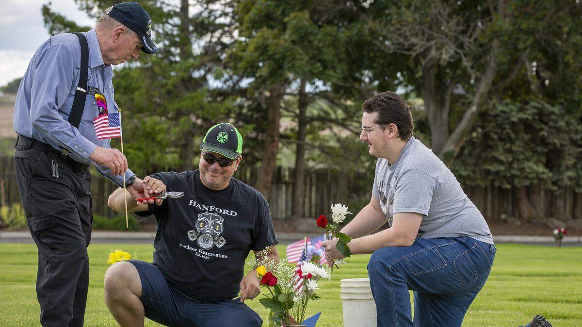 Leon Howard, left, and his son, Rad, and grandson Geoff prepare flowers and flags for Louis D Martin’s grave on Sunday at Sunset Gardens in Richland for Memorial Day. Martin served in the Navy in World War II and was Leon Howard’s stepfather. The Howards also decorated three other graves.