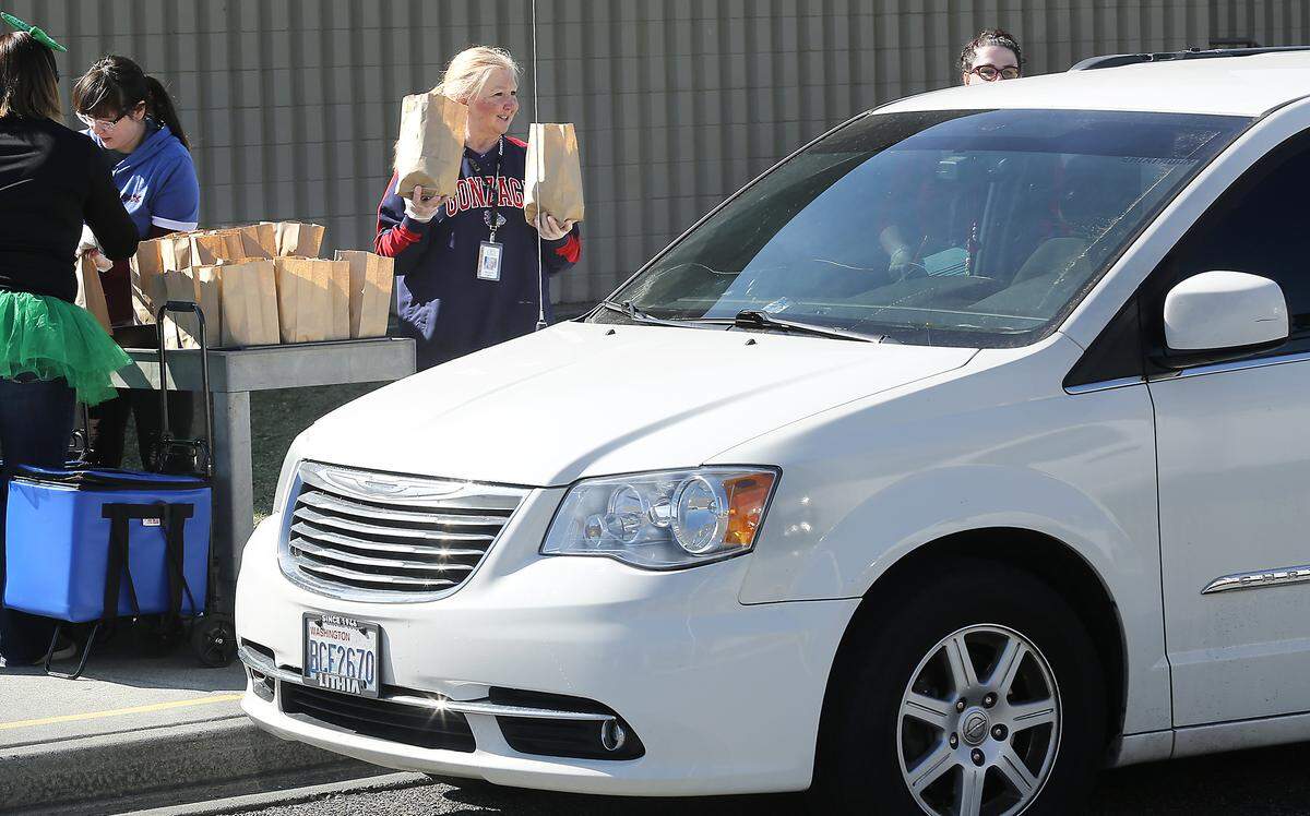 Margie Gourley, lead cook at Ridge View Elemenatry School, helps hand out bagged breakfast and lunch food items to children in a car at the Kennewick school off West 13th Avenue. The meals are being provided each weekday during the school closure for the response to the coronavirus threat. Watch a video at: tricityherald.com/video