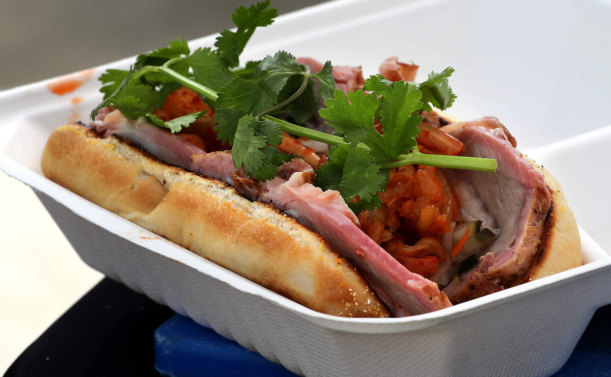 Caleb Ashbeck, owner of Caleb's Sauce Box, offers his signature Pork Bahn Mi sandwich he cooks on his mobile smoker and griddle Friday morning for the opening day of the Richland Farmers Market. The sandwich features sliced marinated pork loin topped with pickled vegetable from another local vendor.