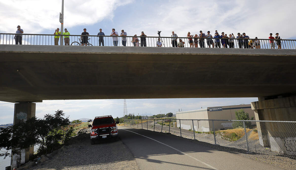 Onlookers line the cable bridge sidewalk after a floatplane crashed into the Columbia River near the Pasco shoreline.
