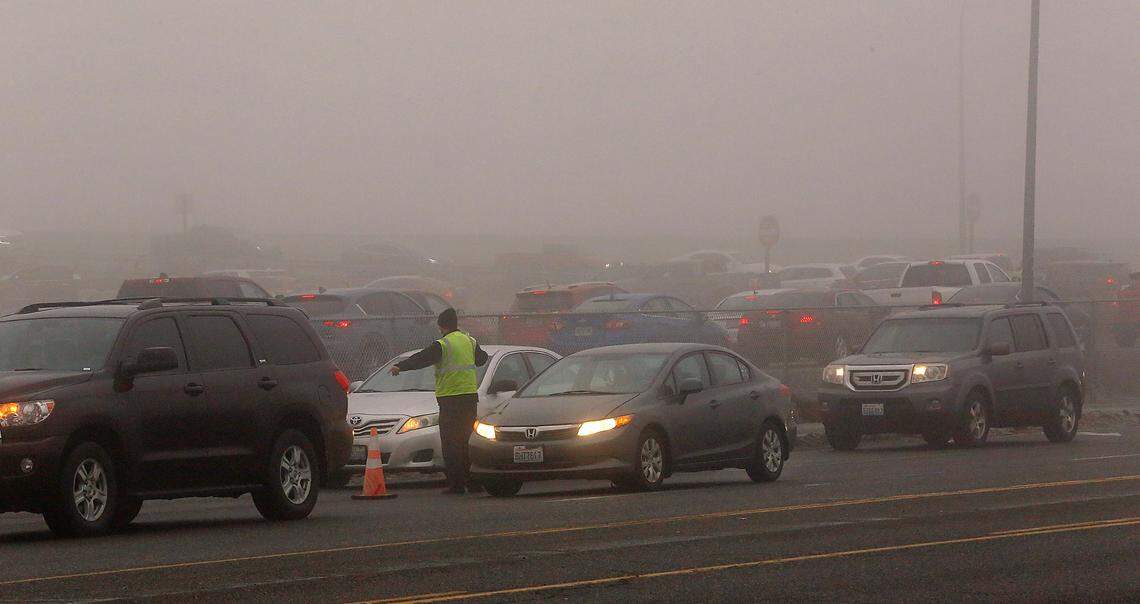 A worker direct drivers into two separate lines Friday morning at they line up on Argent Road waiting to enter the COVID-19 drive-thru testing site at Columbia Basin College in Pasco. Dozens of cars congested the roadway and the highway off-ramp in the foggy conditions.