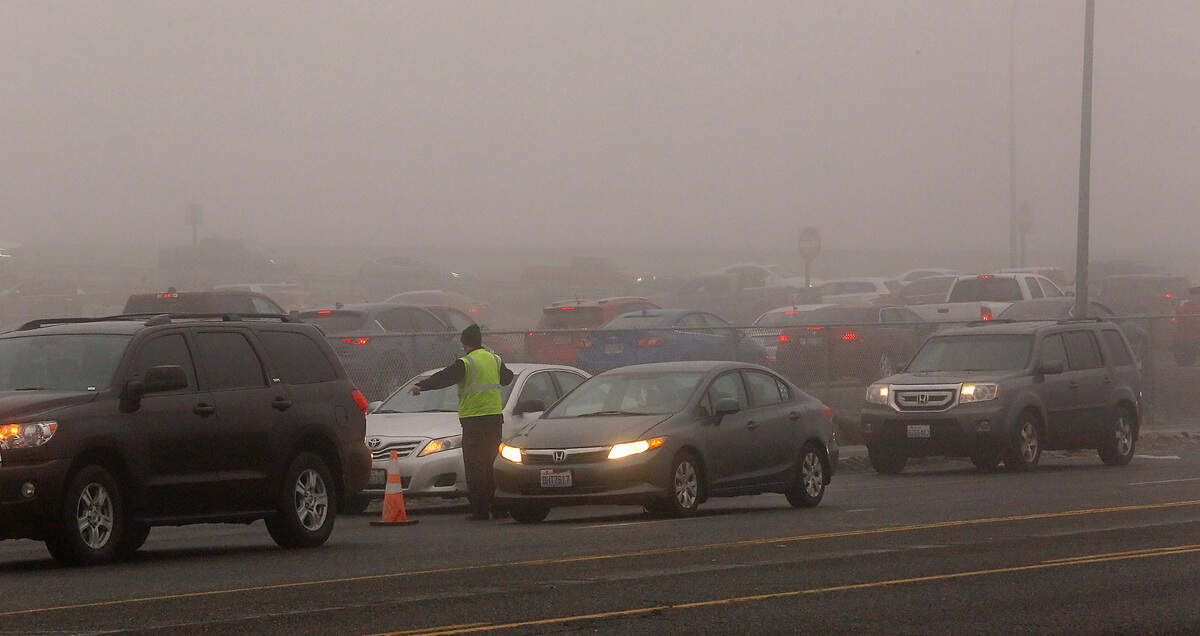 A worker direct drivers into two separate lines Friday morning at they line up on Argent Road waiting to enter the COVID-19 drive-thru testing site at Columbia Basin College in Pasco. Dozens of cars congested the roadway and the highway off-ramp in the foggy conditions.