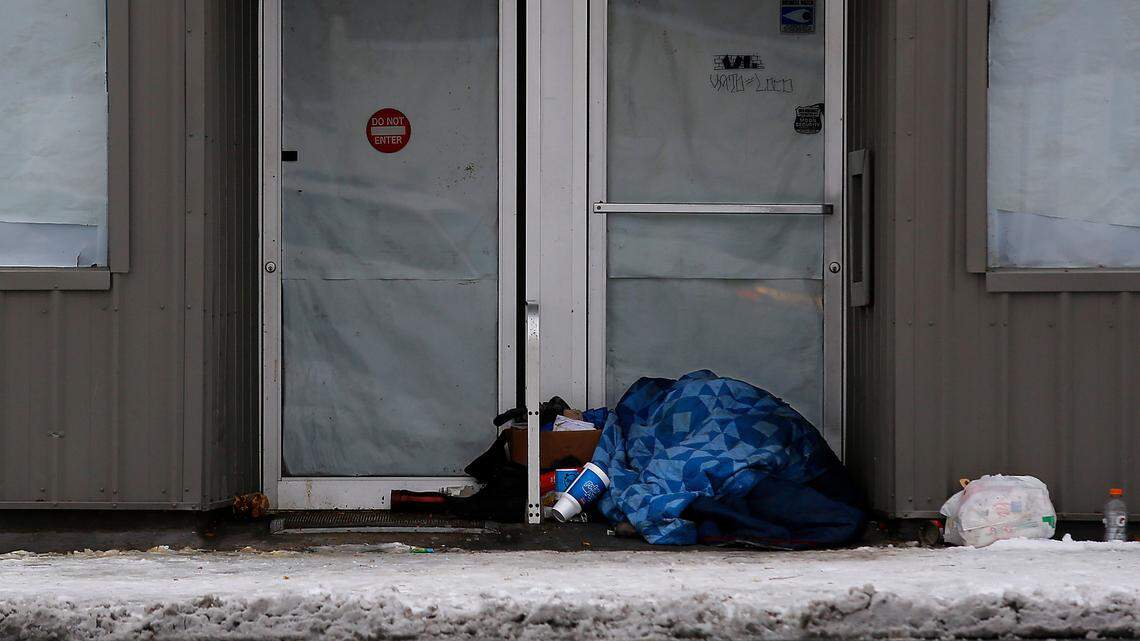 A person sleeps under a blanket with his belongings in the doorway of a closed downtown Kennewick business on a cold morning in December 2022.