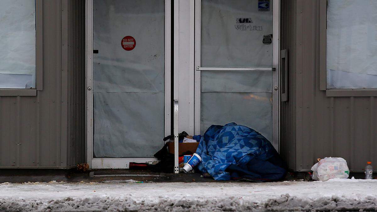 A person sleeps under a blanket with his belongings in the doorway of a closed downtown Kennewick business on a cold morning in December 2022.