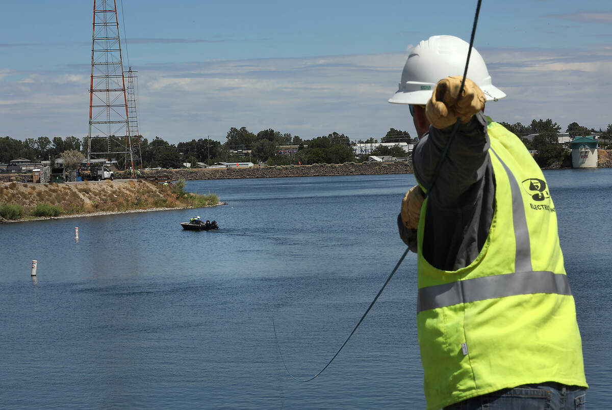A DJ's Electrical Inc. employee holds tension on a rope being pulled across the inlet to Clover Island from the Kennewick shoreline by a work boat as part of the process to replace the high tension power line damaged by last week's plane crash.