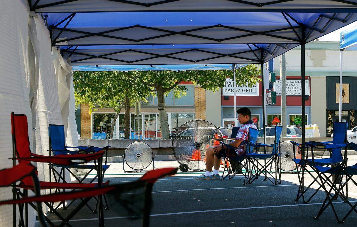 Shane Pace, who is an employee of Jessy and Steve Lee, sits in the shade of 10 pop-up canopies and fans set up in the parking lot at 204 W. Kennewick Ave. in downtown Kennewick as a cooling station during the extreme hot weather that has settled over the Pacific Northwest.
