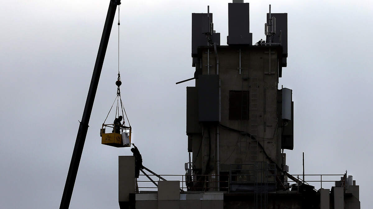 The overcast sky Wednesday morning provides a muted backdrop for a two-man crew, one suspended in a bucket held aloft by a crane, working on cell phone equipment to top of the former grain elevator on West Clearwater Avenue in west Kennewick.