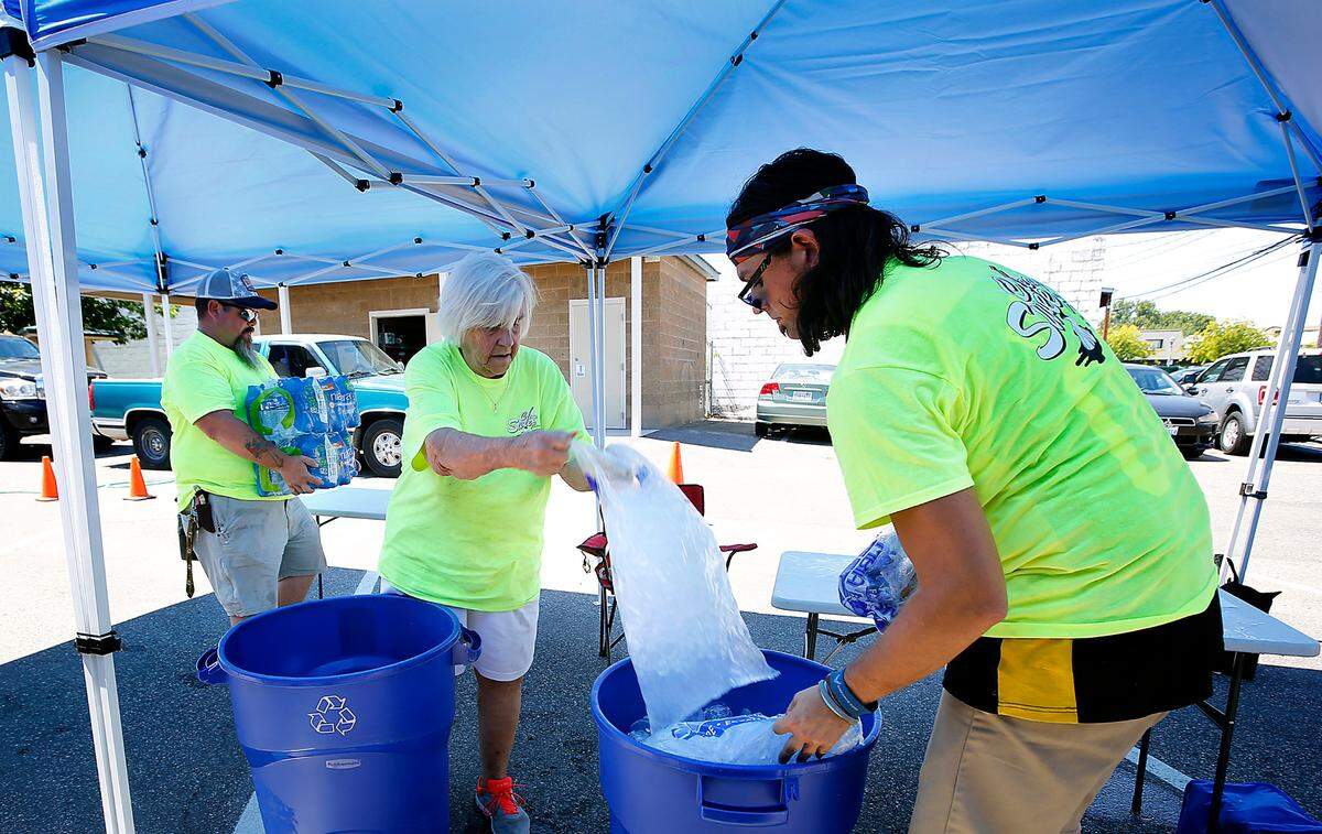 Clean Sweep Tri-Cities volunteers Matt McKee, Lynne Mckee and Brian Bartlett, from left, add ice and bottled water to barrels in June 2021 at the shade station set up in downtown Kennewick.