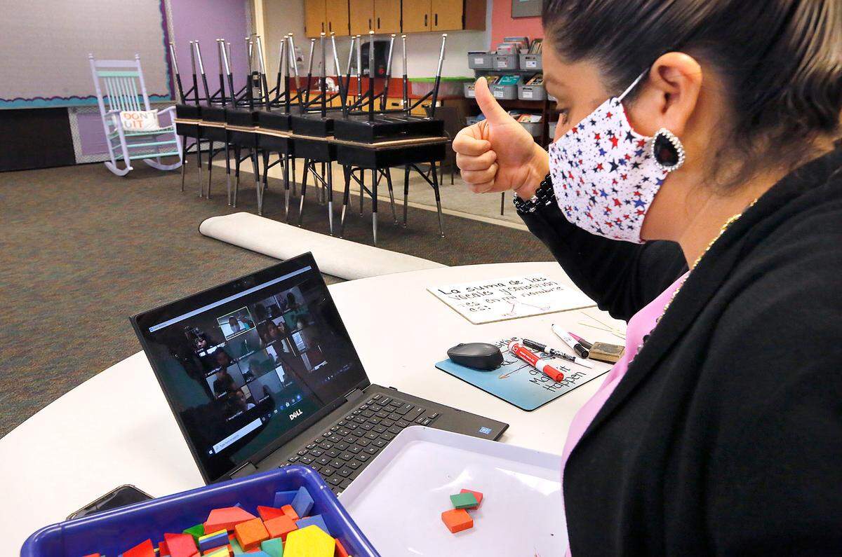 Second-grade teacher Esmeralda Villegas gives a thumbs up to students on her computer screen while conducting an online video class session from her room at Captain Gray STEM Elementary School in Pasco. The desks and chairs in her room are stacked off to the side for now.