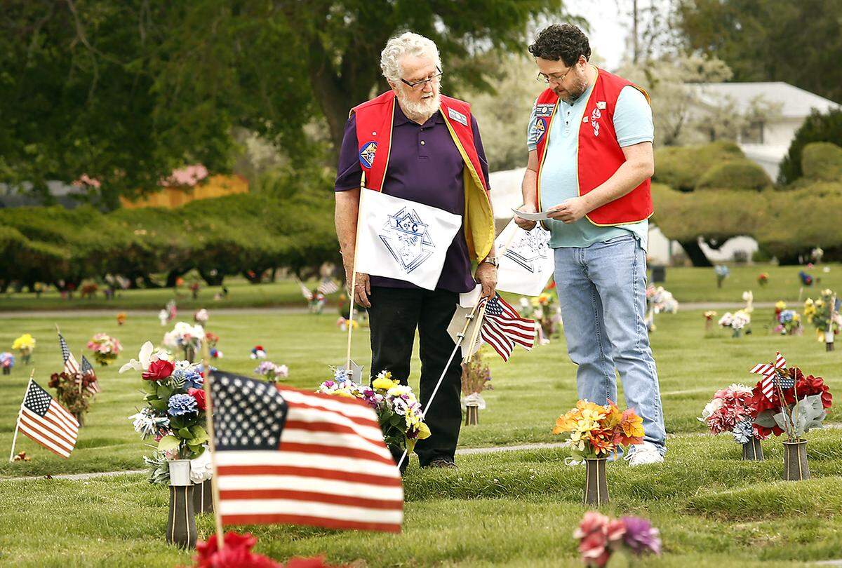 2020 FILE PHOTO — Pat McCabe, left, and his son, Andrew, with Knights of Columbus at the Parish of the Holy Spirit Catholic Church in Kennewick, refer to a list of names while placing flags on graves at Desert Lawn Memorial Park.
