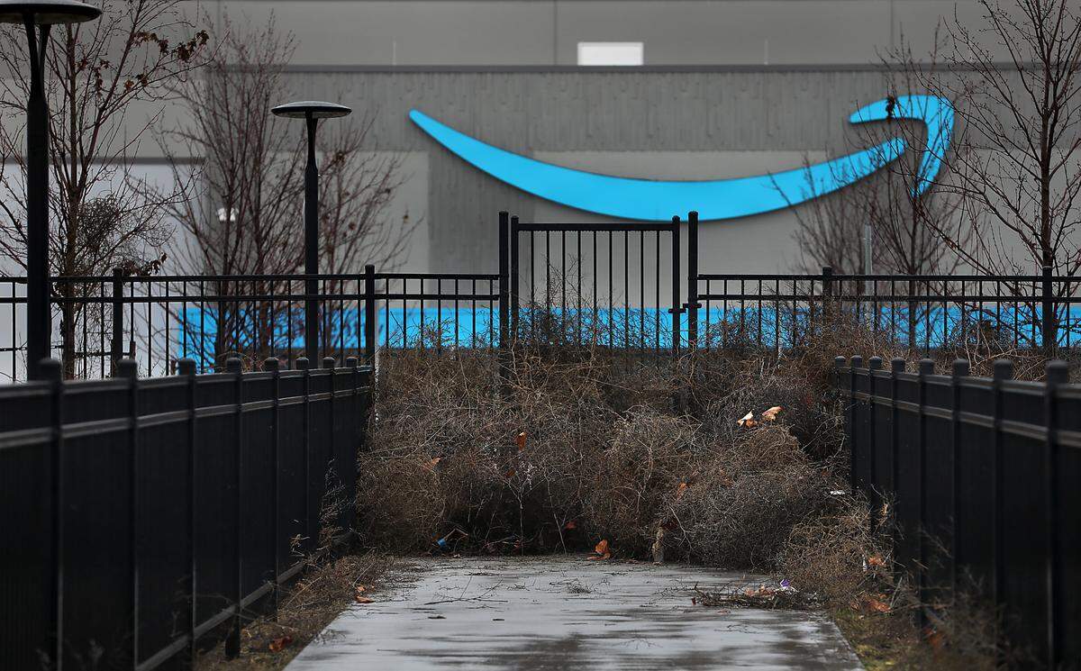 Tumbleweeds, leaves and other debris clog a pedestrian gate and sidewalk near the main entryway to one of two massive, never-opened Amazon distribution centers in Pasco.
