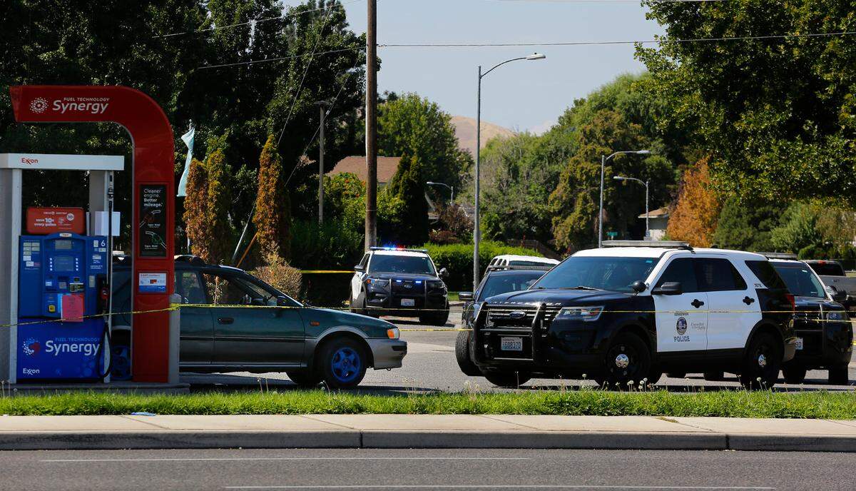 As investigators document the scene, vehicles from the Kennewick Police Department and the Benton County Sheriff’s Office remain behind crime scene tape parked near a four-door Subaru at the gas pumps.