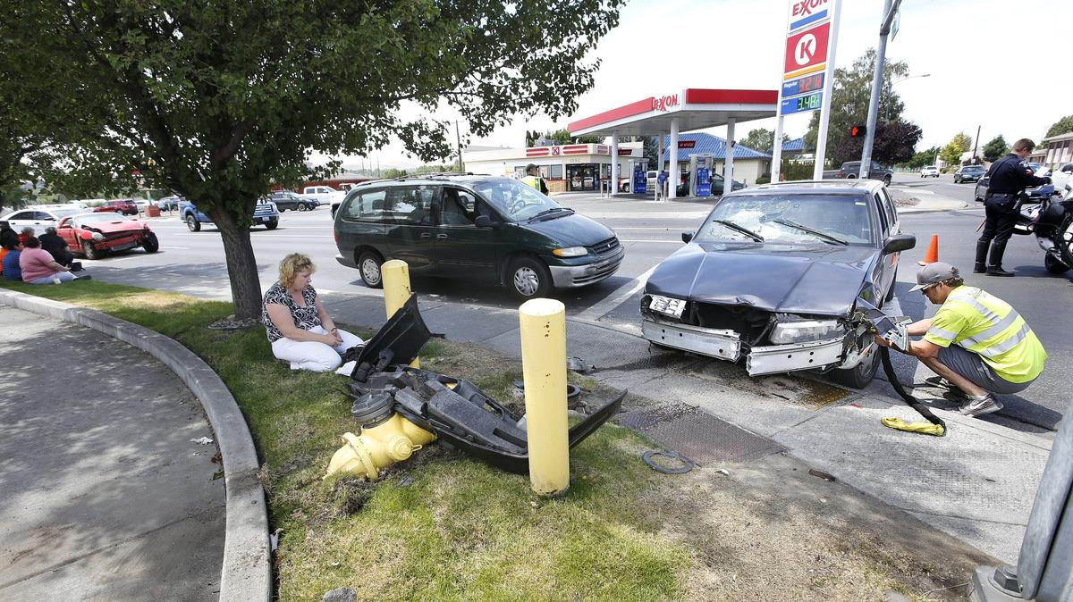 Karla Beck, left, of Kennewick sits in the shade Friday as tow truck driver Kolton Dean of Mid-Columbia Towing prepares to remove her damaged Volvo 960 from the intersection of West 10th Avenue and South Washington Street.