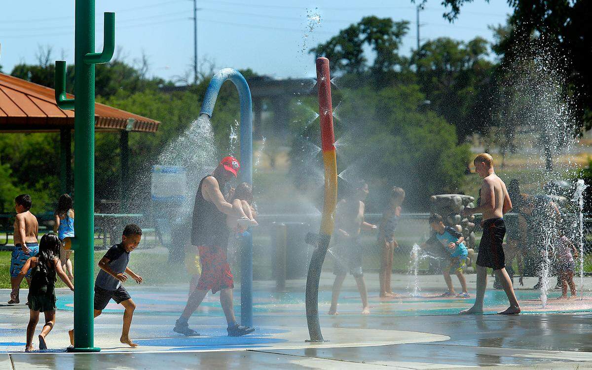 Children and adults cool off under the sprayers at the splash pad at the Playground of Dreams in Kennewick’s Columbia Park.