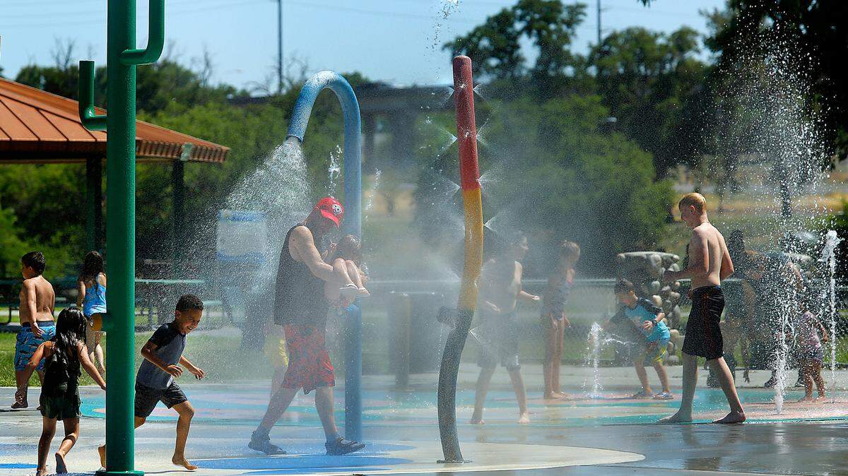 Children and adults cool off under the sprayers at the splash pad at the Playground of Dreams in Kennewick’s Columbia Park.