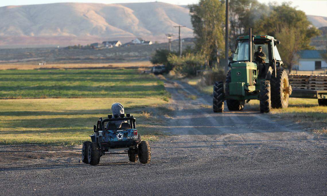 Ashley Cox’s son, Brody, 3, drives his battery-powered toy jeep to see a neighbor as a tractor heads out to bring pumpkins in from the fields at the Robert S. Cox Farms.