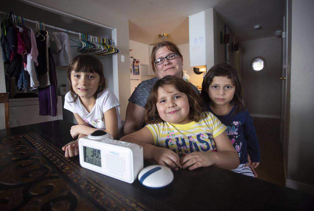 Heidi Cruz sits with her three daughters Mariela, 8, left, Adriana, 6, center, and Christina, 5, and the Lifetone Bedside Clock and Vibrating Fire Alarm that can shake them if there’s a fire in the house.
