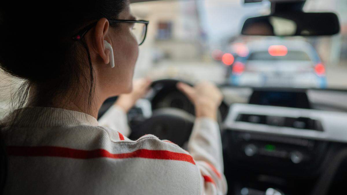 Close-up shot of woman sitting in driver’s seat in her car with earbuds in.