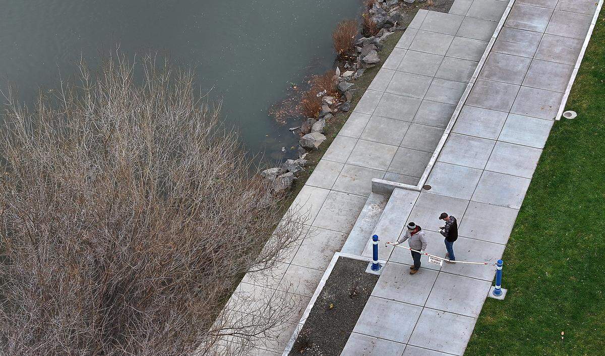 Pulbic works employees Sam Clements, left, and Tyler Klages, place the "Pathway Closed" sign and barricade Tuesday morning along the Yakima River shoreline at West Richland's Yakima Gateway Park. 
