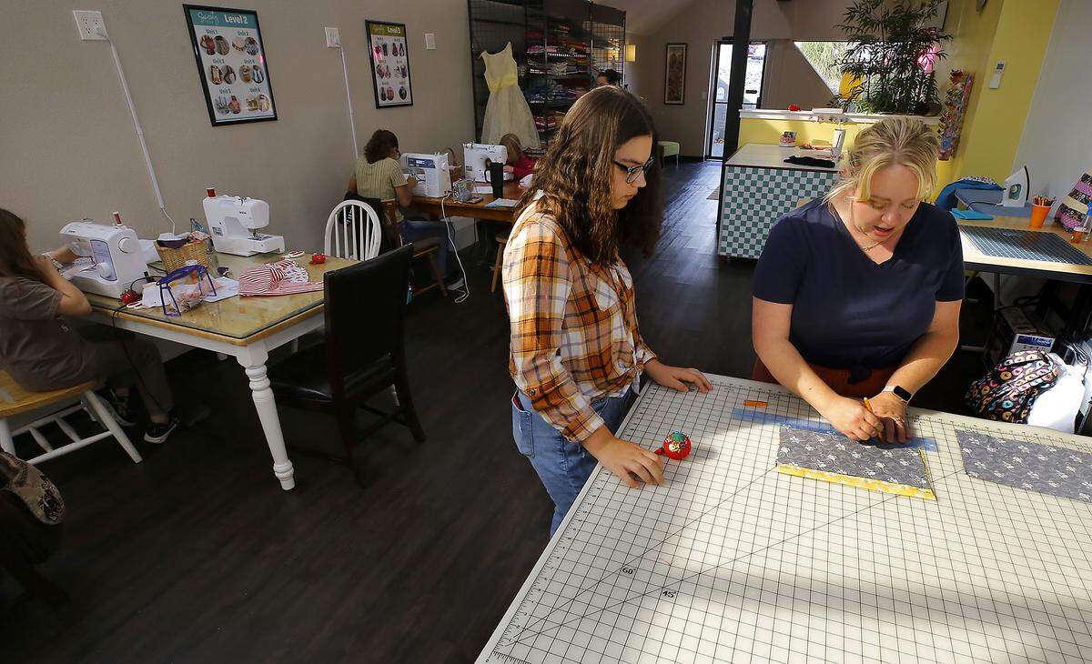 Jessica Beck, owner of Jessica's Sewing School, helps student  Lucca Taranto, 15, work at cutting fabric for the next step of her project.