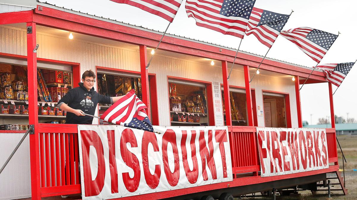 Jordan Huenergardt, 16, unfurls United States flags Tuesday morning helping his father, Doug, open the fireworks stand in Burbank for the final hours of New Year’s Eve 2019 sales.