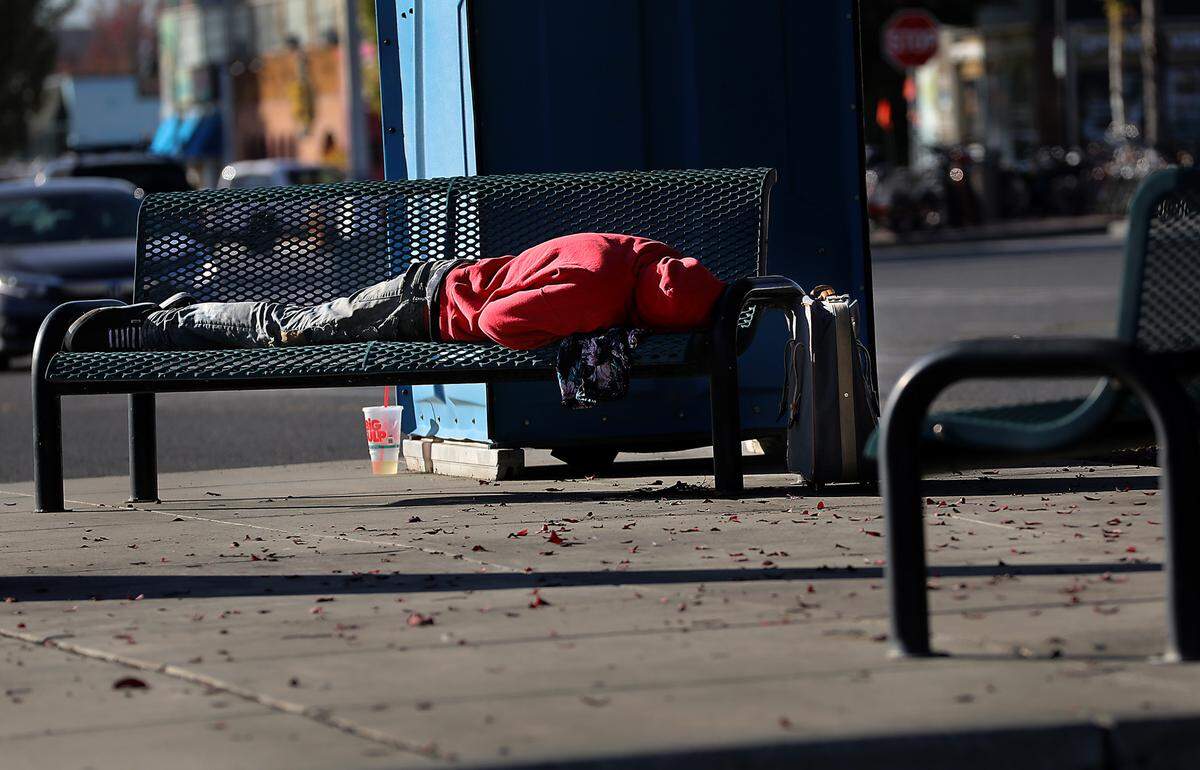 An apparent homeless person sleeps on a bench in the parking lot of the Uptown Shopping Center in Richland in October 2023.
