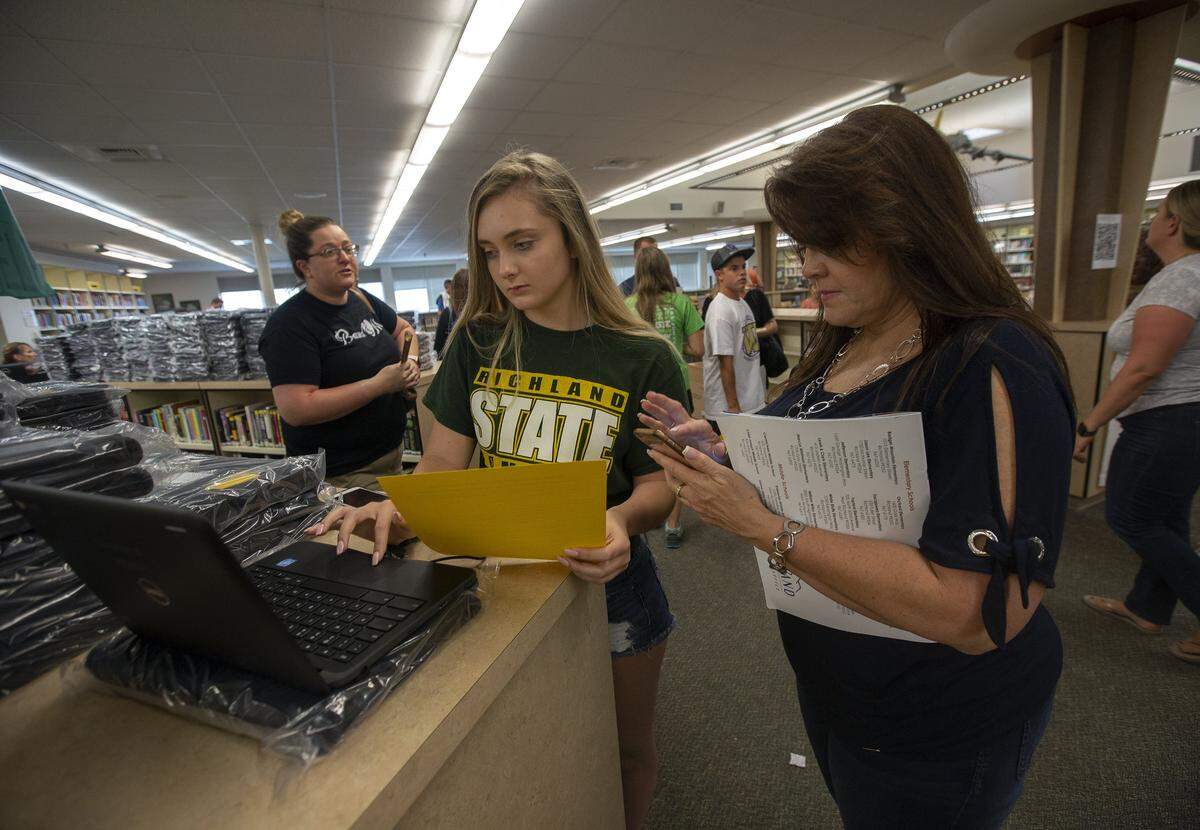 Richland High sophomore Natasha Ford, center, checks to make sure her new Google Chromebook is working properly with her mother, Darla Ford, in August during registration at the school.