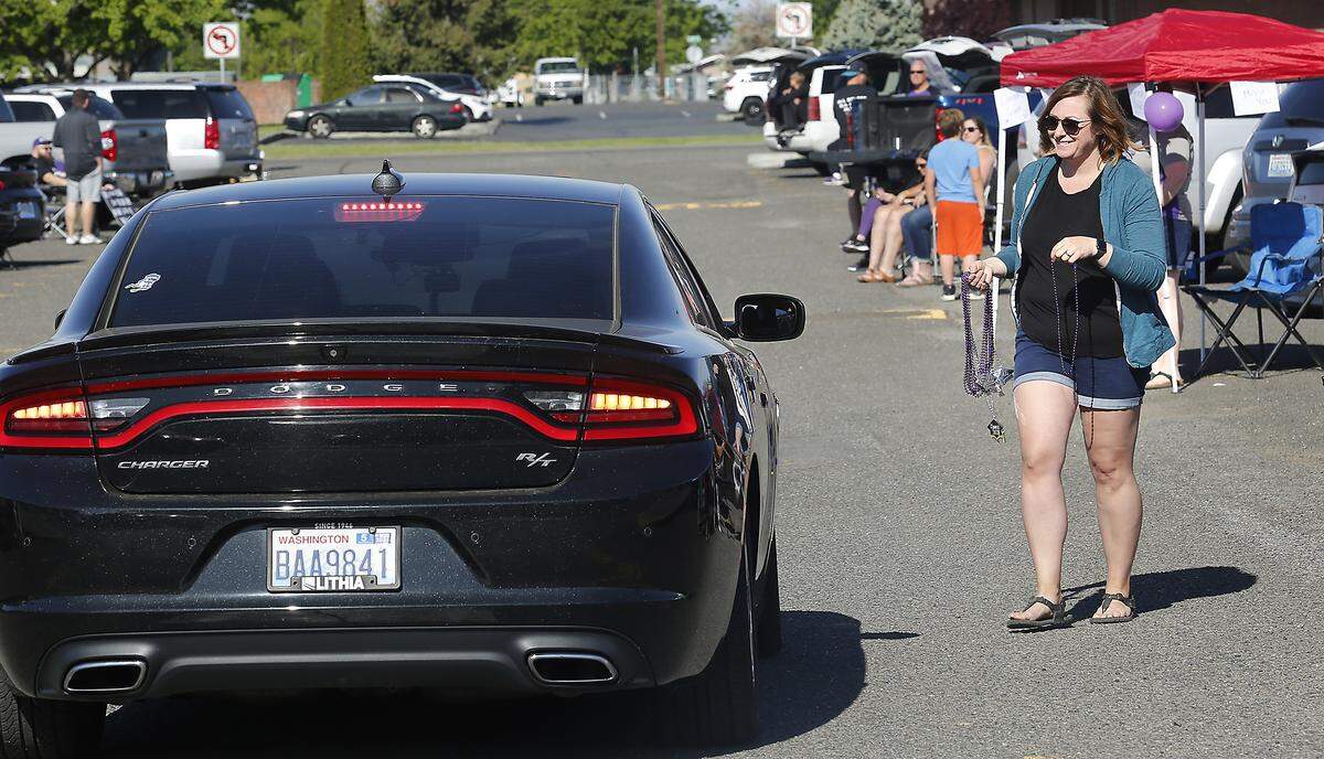 Pasco High teacher Megan Williams hands out colorful party necklaces in the “cheer zone” of Friday’s cap and gown distribution the the school’s 2020 seniors in the school’s parking lot. Williams used a no-contact exchange by hanging the necklace on the car’s sideview mirrors. Watch a video at: tricityherald.com/videos