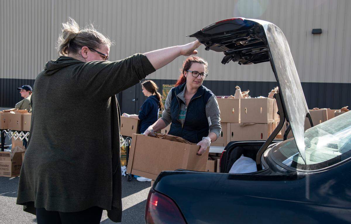 Volunteers Lisa Sanders, left, and Abby Grisham, right, load boxes of food into cars during Second Harvest’s drive-thru food distribution March 24, 2020.