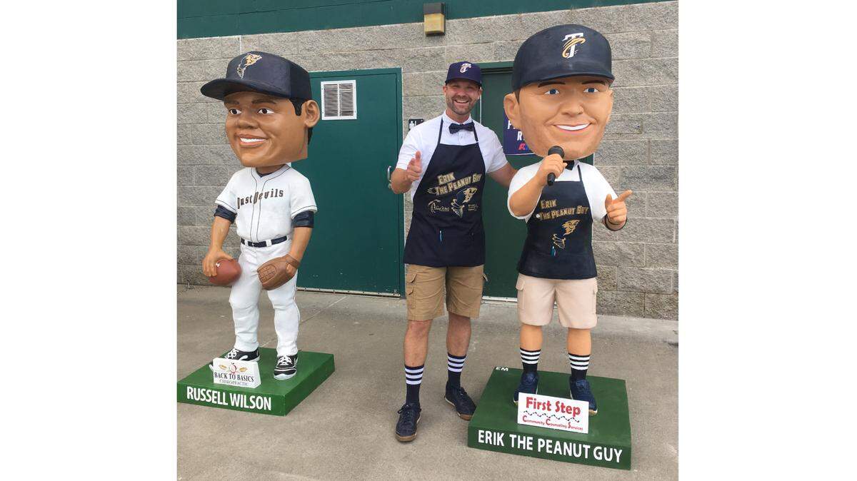 Erik Mertens, also known as Erik The Peanut Guy, stands next to the gigantic bobblehead of himself that the Tri-City Dust Devils had made in his honor recently. At left is the giant bobblehead of Russell Wilson, who is now the quarterback of the Seattle Seahawks. Wilson played for the Dust Devils in 2010.