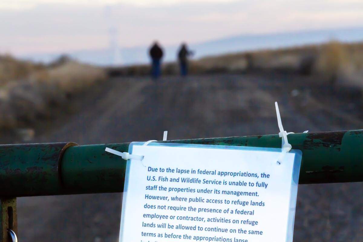 Two people walk on a trail past a gate with a government shutdown sign at McNary National Wildlife Refuge near Burbank.