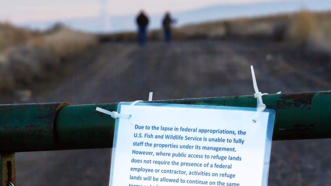 Hikers take a walk on a trail past a gate with a government shutdown sign at McNary National Wildlife Refuge near Burbank.