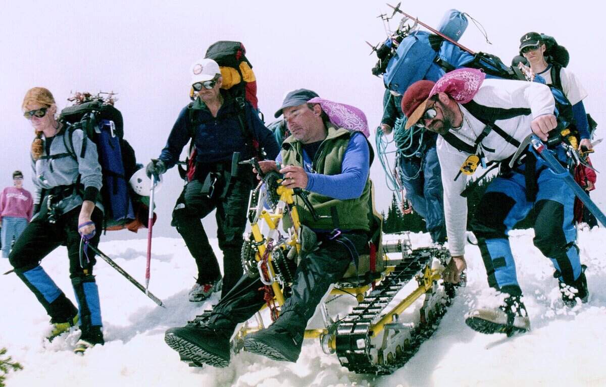 Pete Rieke cranks over the last little slope as he speeds the tracks toward the Paradise parking lot in Mount Rainier National Park in June 2000, after spending 13 days on the mountain. From left, Linda Soper, Bob Bass and Paul Soboleski pace Rieke into the parking lot where they met family and friends. Rieke, 43, a research chemist from Pasco who lost use of his legs in a 1994 rock climbing accident, began his ascent June 8 at the 5,240-foot level using a hand-cranked ’snow pod’ he designed and built.