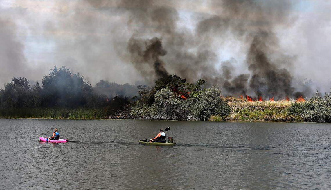 Kayakers Eileen Freeman, left, and Gene Rabung paddle past smoke and flames as Bateman Island burned in September 2023 for the second time that year.