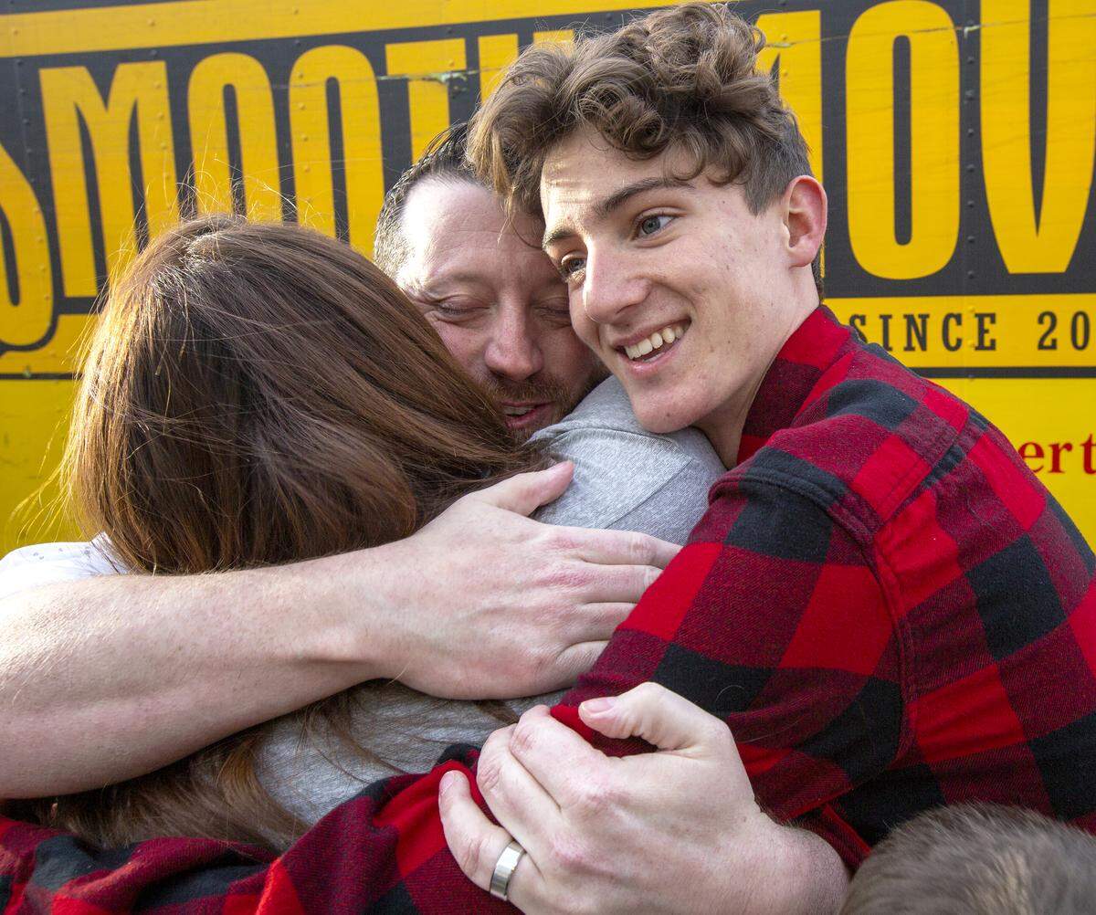 Christina Lopez, left, and Tyler Lopez, right, hug Travis Newby, center, a Lewis and Clark Elementary School teacher, who helped organize a massive drive to help the Lopez family after their house burned down prior to Thanksgiving.