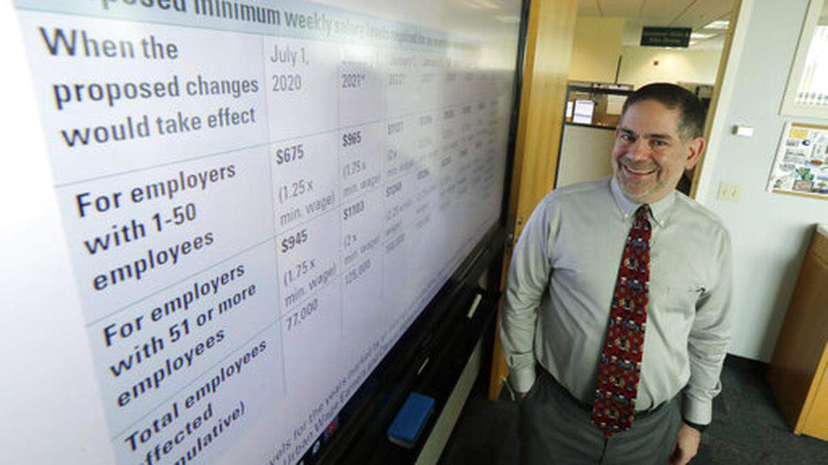 Joel Sacks, director of the Washington state Department of Labor and Industries, poses for a photo, Wednesday, June 5, 2019, in his office in Tumwater, Wash., next to a an information sheet showing how more than 250,000 workers in Washington state would be newly eligible for overtime pay by 2026 under a rule proposed Wednesday by L&I. (AP Photo/Ted S. Warren)